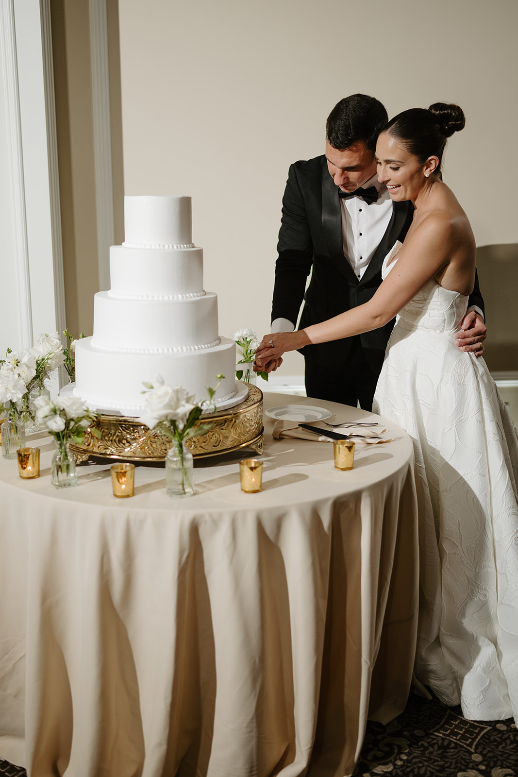 Bride and groom holding the knife together as they slice into their elegant white wedding cake.